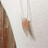 a closeup of the Binary Necklace by Third & Co. Studio: Agate "tooth" and tube shape in cream peach mauve orange, minimalist design with Sterling Silver snake chain lariat style long length