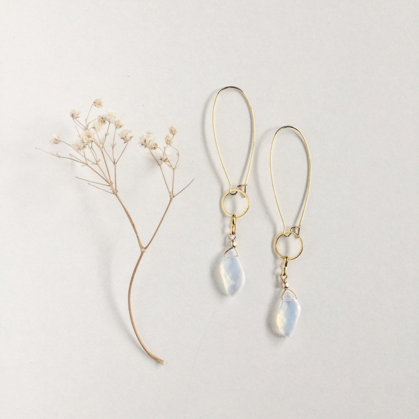 model wearing the Aurora Earrings by Third & Co. Studio: faceted synthetic wavy-shaped Opalite in clear and blue flashing rainbow colors, small sections of gold plated vintage circle geometric chain, gold-plated stainless steel ear wires, lightweight sparkly statement earrings shown against a white background and dried baby's breath flowers