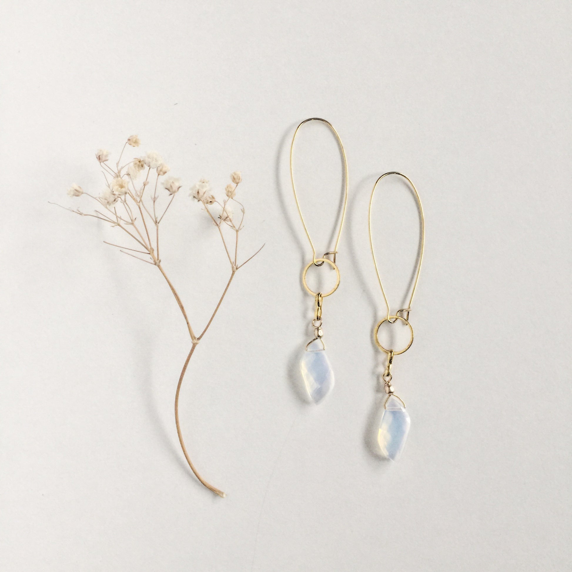 model wearing the Aurora Earrings by Third & Co. Studio: faceted synthetic wavy-shaped Opalite in clear and blue flashing rainbow colors, small sections of gold plated vintage circle geometric chain, gold-plated stainless steel ear wires, lightweight sparkly statement earrings shown against a white background and dried baby's breath flowers