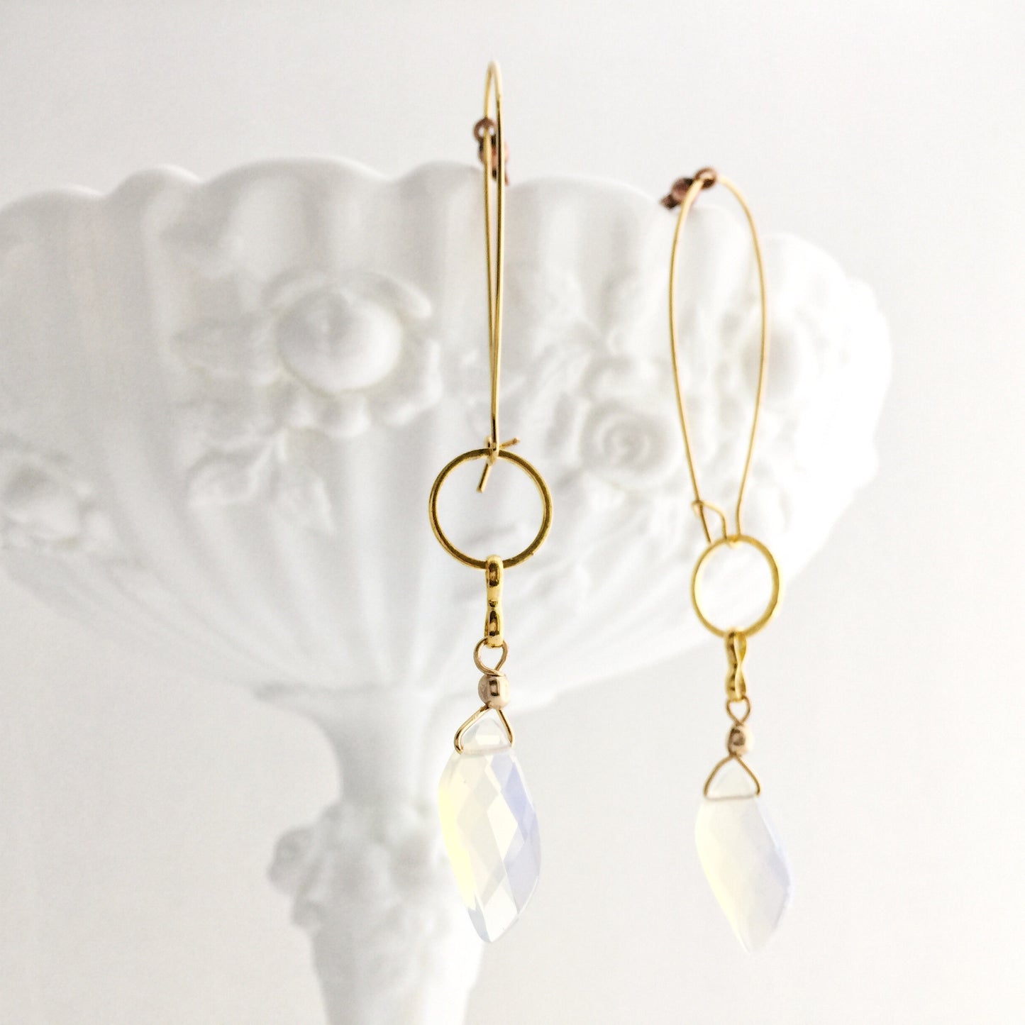 model wearing the Aurora Earrings by Third & Co. Studio: faceted synthetic wavy-shaped Opalite in clear and blue flashing rainbow colors, small sections of gold plated vintage circle geometric chain, gold-plated stainless steel ear wires, lightweight sparkly statement earrings, shown hanging from a white dish against a white background