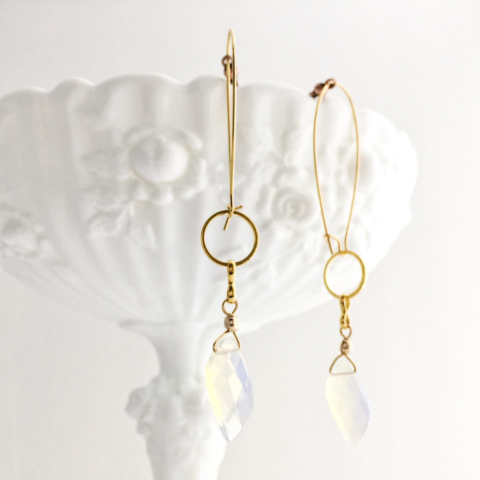 model wearing the Aurora Earrings by Third & Co. Studio: faceted synthetic wavy-shaped Opalite in clear and blue flashing rainbow colors, small sections of gold plated vintage circle geometric chain, gold-plated stainless steel ear wires, lightweight sparkly statement earrings, shown hanging from a white dish against a white background