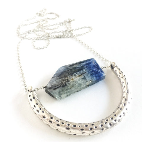 The Ara Necklace by Third & Co. Studio: a single flat irregular-shaped Kyanite nugget in blue gray and black, silver plated crescent shape with oxidized spots, and nickel-free silver plated chain long 32" length, shown against a plain white background