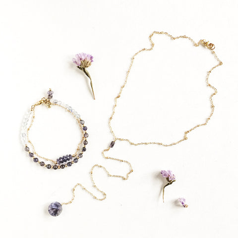 Andromeda Necklace by Third & Co. Studio; faceted and round blue Iolite, gold plated satellite chain lariat necklace with lobster claw clasp, shown against a white background as a matching set with the Andromeda Bracelet