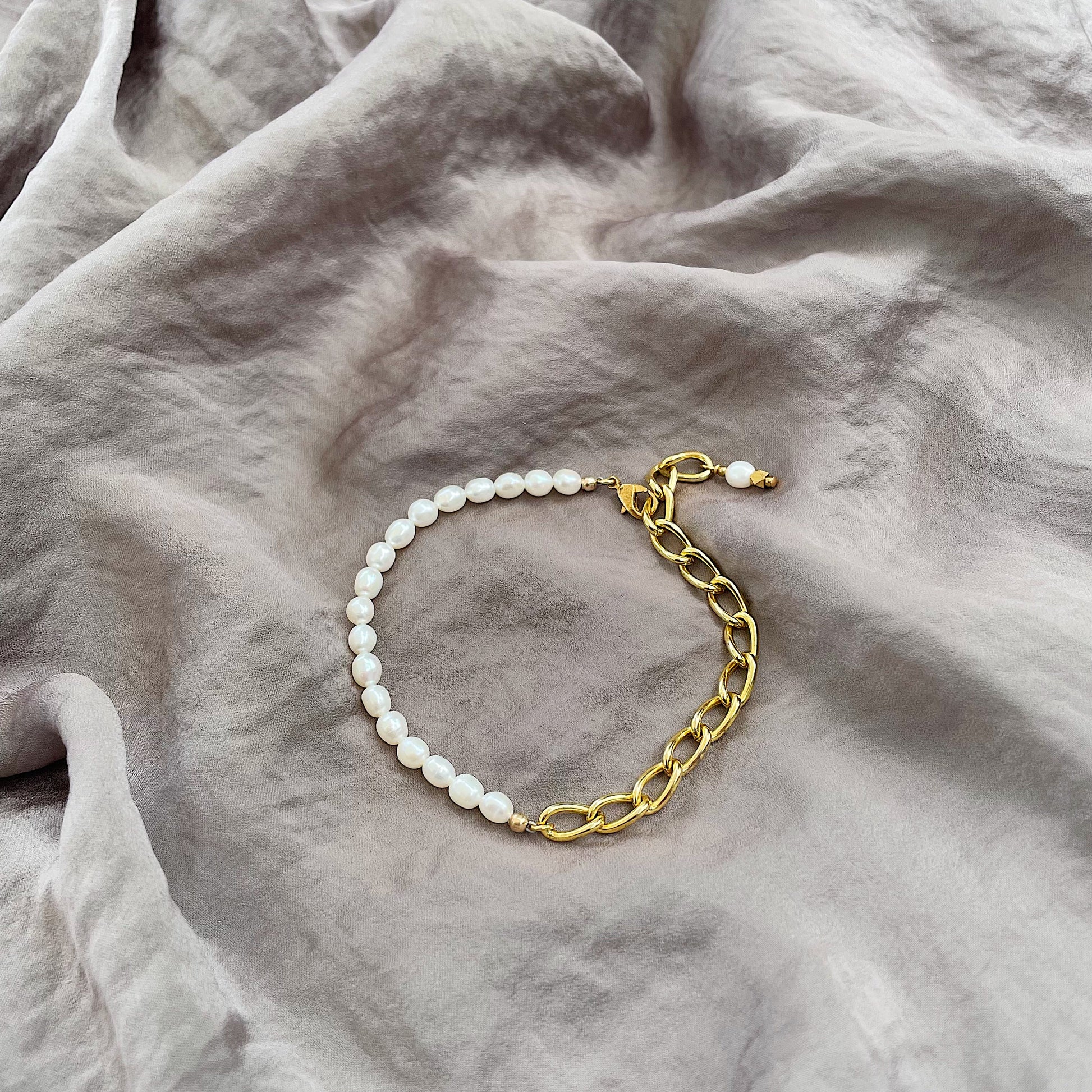 a model wearing the Aletta Bracelet from Third & Co. Studio with white fresh water pearl, gold plated vintage chain with adjustable length and lobster claw clasp against a silky gray fabric backgrou