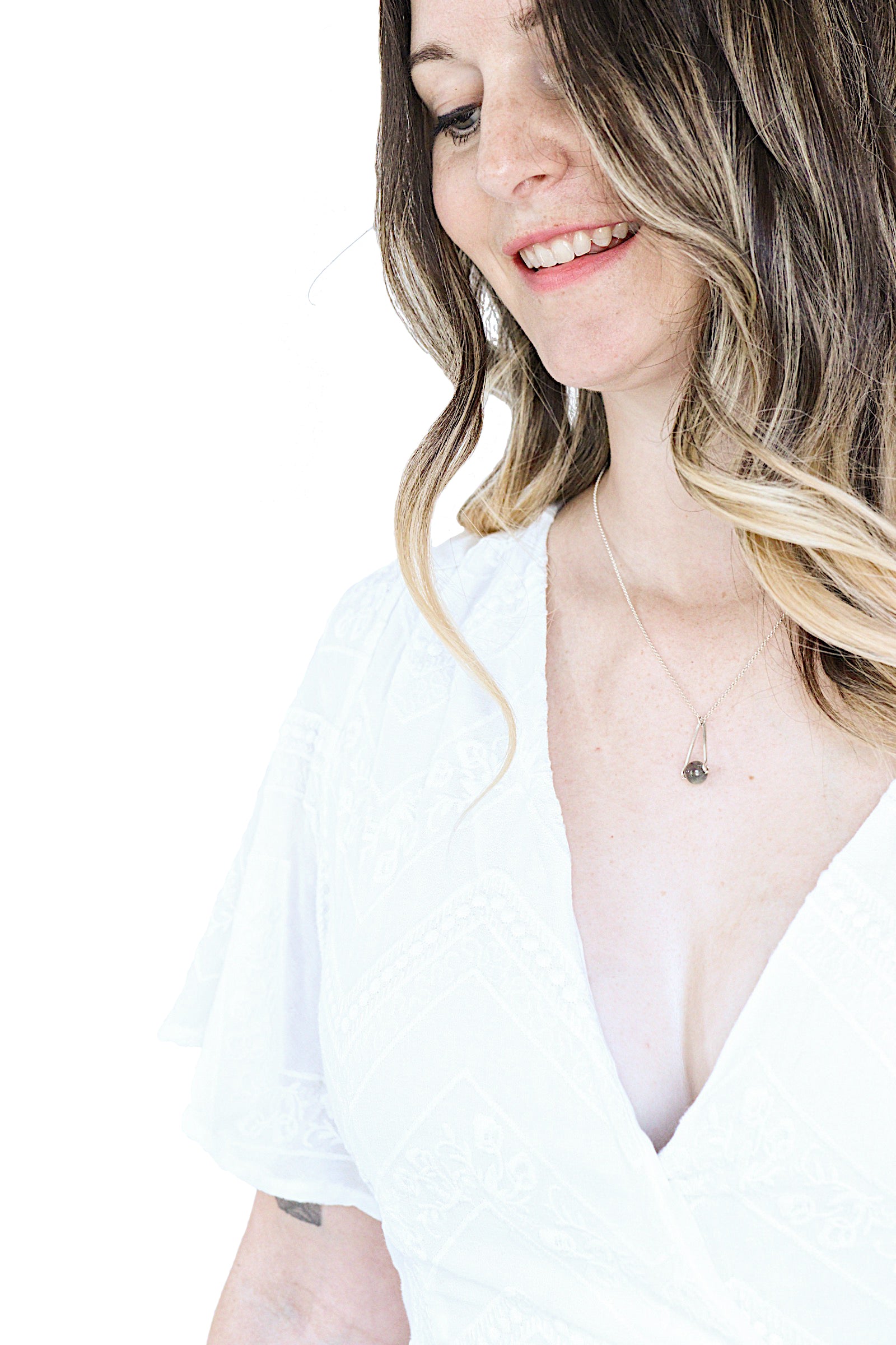 model in a white top and long hair wearing Labradorite round in green gray with flashing blue, sterling silver elongated triangle shape, sterling silver chain short necklace with white background
