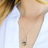 model in a white top wearing a Labradorite round in green gray with flashing blue, sterling silver elongated triangle shape, sterling silver chain short necklace