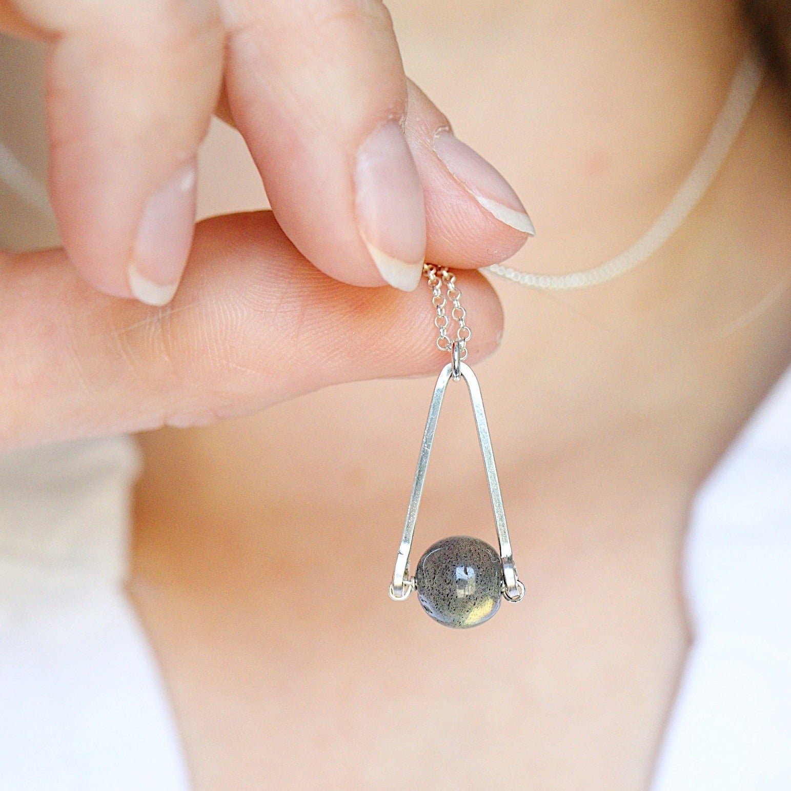model holding a Labradorite round in green gray with flashing blue, sterling silver elongated triangle shape, sterling silver chain short necklace