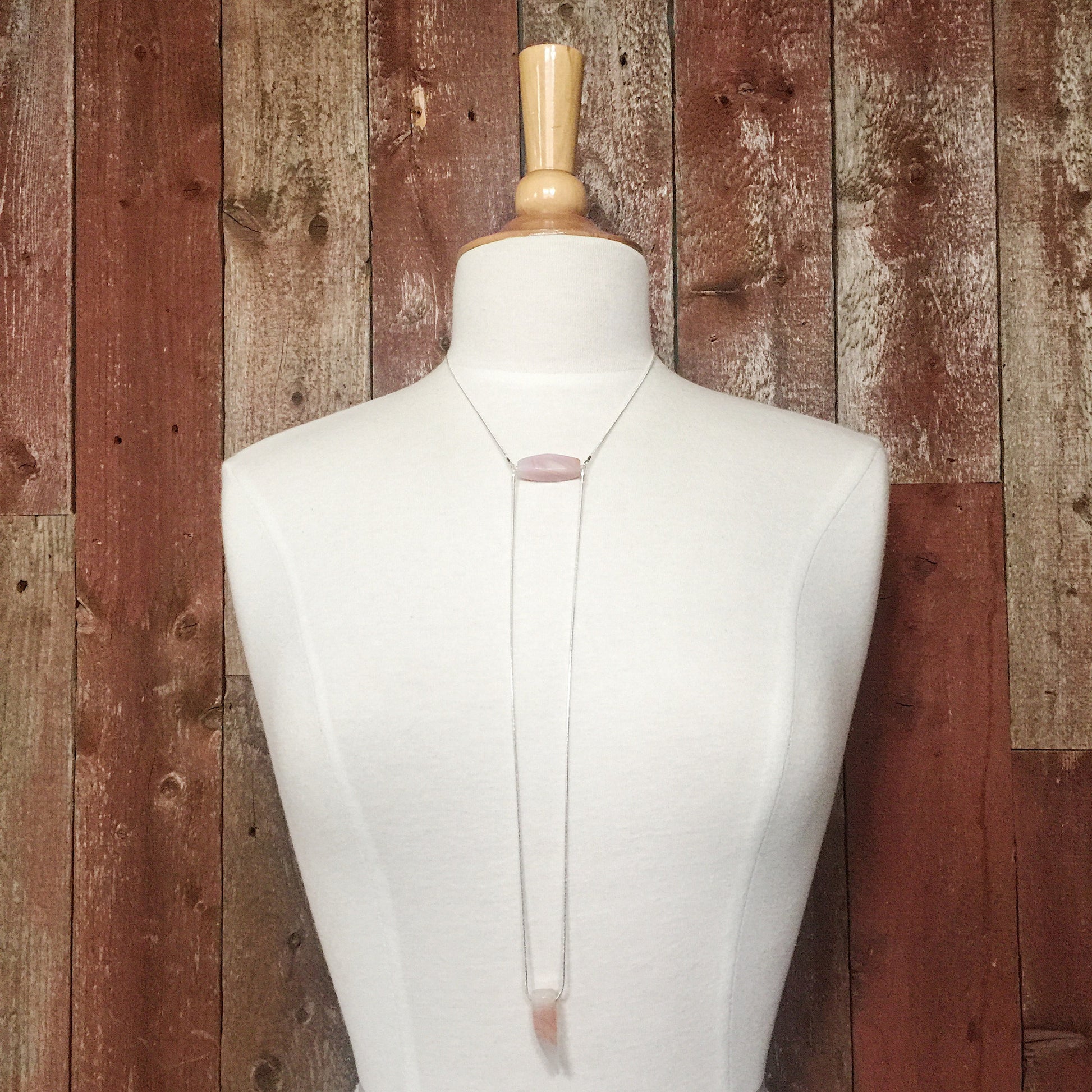 mannequin wearing the Binary Necklace by Third & Co. Studio: Agate "tooth" and tube shape in cream peach mauve orange, minimalist design with Sterling Silver snake chain lariat style long length, shown against a rustic red background