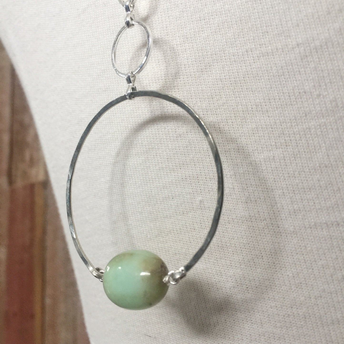 closeup of the Apogee Necklace by Third & Co. Studio; light green and brown Chrysophase flat oval, vintage silver circle & oval chain, silver plated nickel-free chain, hammered German silver nickel circle, shown on a beige mannequin