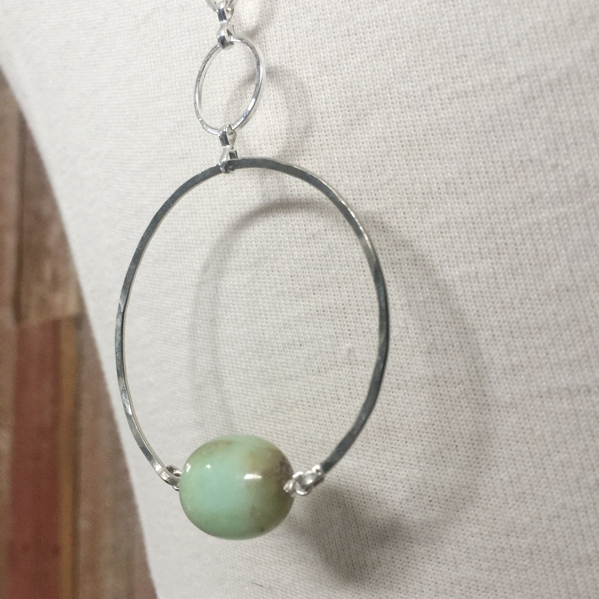 closeup of the Apogee Necklace by Third & Co. Studio; light green and brown Chrysophase flat oval, vintage silver circle & oval chain, silver plated nickel-free chain, hammered German silver nickel circle, shown on a beige mannequin