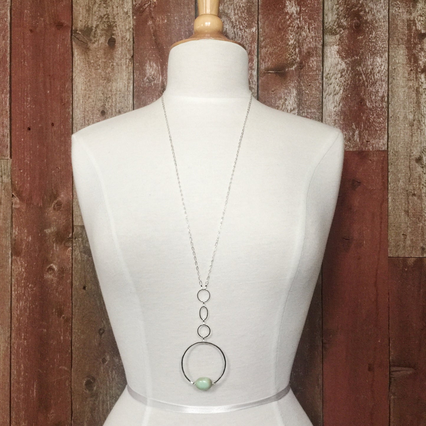 Apogee Necklace by Third & Co. Studio; light green and brown Chrysophase flat oval, vintage silver circle & oval chain, silver plated nickel-free chain, hammered German silver nickel circle, shown on a beige mannequin and rustic red backdrop