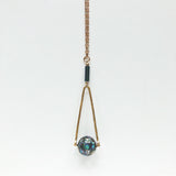 Round Abalone "disco ball" in green, black, cream, tan, brown, and blue with elongated hammered brass triangle frame, gray Hematite round tube, and gold plated nickel-free chain long lnegth 30" chain necklace on white background