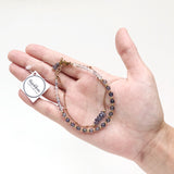 a model holding in hand the Andromeda Bracelet by Third & Co. Studio; faceted blue Iolite, round clear and blue Quartz and Iolite, gold plated satellite chain adjustable length bracelet with lobster claw clasp, shown against a white background