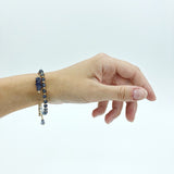 a model wearing the Andromeda Bracelet by Third & Co. Studio; faceted blue Iolite, round clear and blue Quartz and Iolite, gold plated satellite chain adjustable length bracelet with lobster claw clasp, shown against a white background