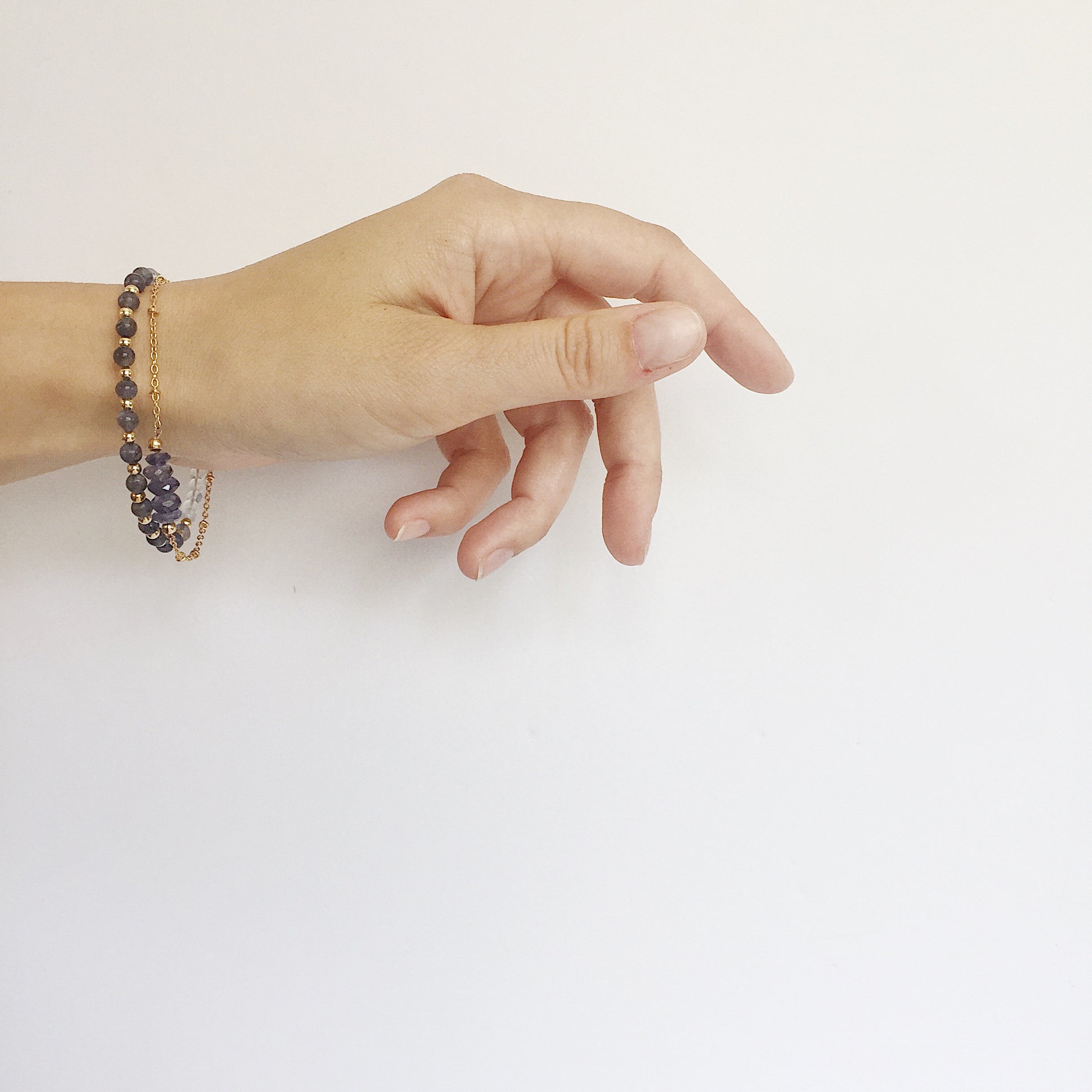 model wearing the Andromeda Bracelet by Third & Co. Studio; faceted blue Iolite, round clear and blue Quartz and Iolite, gold plated satellite chain adjustable length bracelet with lobster claw clasp, shown against a white background