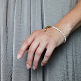 a model wearing the Aletta Bracelet from Third & Co. Studio with white fresh water pearl, gold plated vintage chain with adjustable length and lobster claw clasp hanging down, against a silky gray fabric backgrou