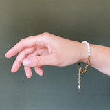 a model wearing the Aletta Bracelet from Third & Co. Studio with white fresh water pearl, gold plated vintage chain with adjustable length and lobster claw clasp hanging down, against a green background