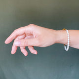 a model wearing the Aletta Bracelet from Third & Co. Studio with white fresh water pearl, gold plated vintage chain with adjustable length and lobster claw clasp, against a green backgrou