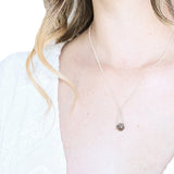 model with a white top and long hair wearing a Labradorite round in green gray with flashing blue, sterling silver elongated triangle shape, sterling silver chain short necklace with white background