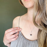 model in a gray dress and long hair wearing a Labradorite round in green gray with flashing blue, sterling silver elongated triangle shape, sterling silver chain short necklace wuth green backgound