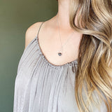 model in gray dress and long hair wearing a Labradorite round in green gray with flashing blue, sterling silver elongated triangle shape, sterling silver chain short necklace against a green background