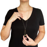 a model in a black v-neck dress wearing and holding a Round Labradorite in green, gray and flashes of blue with an elongated triangular hammered brass frame, a small vintage bar accent and 14K gold fill chain 30" length necklace