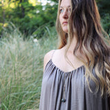model with gray dress and long hair wearing a Round Labradorite in green, gray and flashes of blue with an elongated triangular hammered brass frame, a small vintage bar accent and 14K gold fill chain 30" length necklace